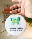 This is a 4 inch embroidery hoop with white fabric and a green and mint butterfly embroidered in the center. under the butterfly is a baby name stitched in black with the date underneath.