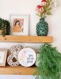 Embroidery hoop on a shelf that has rainbow pastel butterflies stitched into the fabric with the text, "you are so loved"