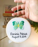 This is a 4 inch embroidery hoop with white fabric and a green and mint butterfly embroidered in the center. under the butterfly is a baby name stitched in black with the date underneath. 